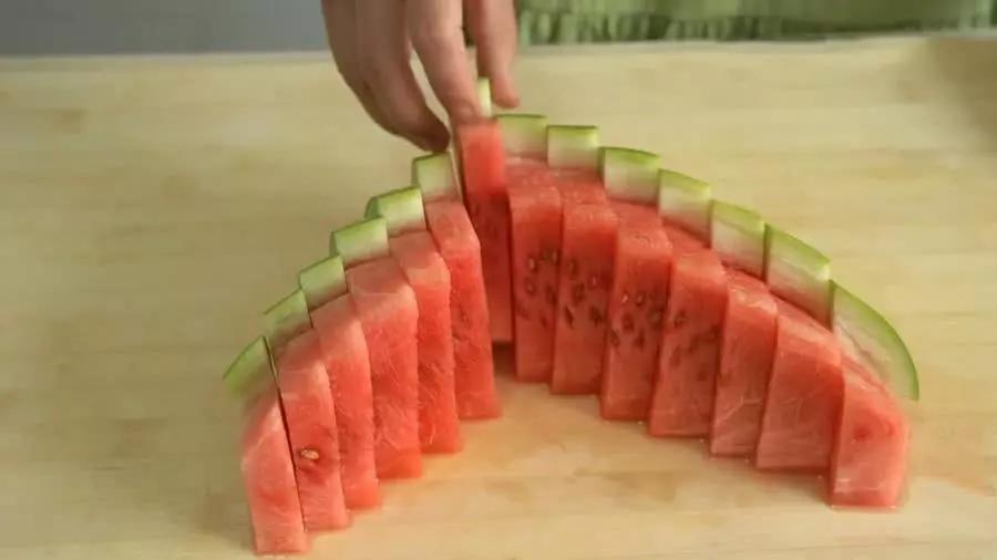 把另一半西瓜切成两半,用小刀在两边横着划一刀,再竖着切几刀,最后