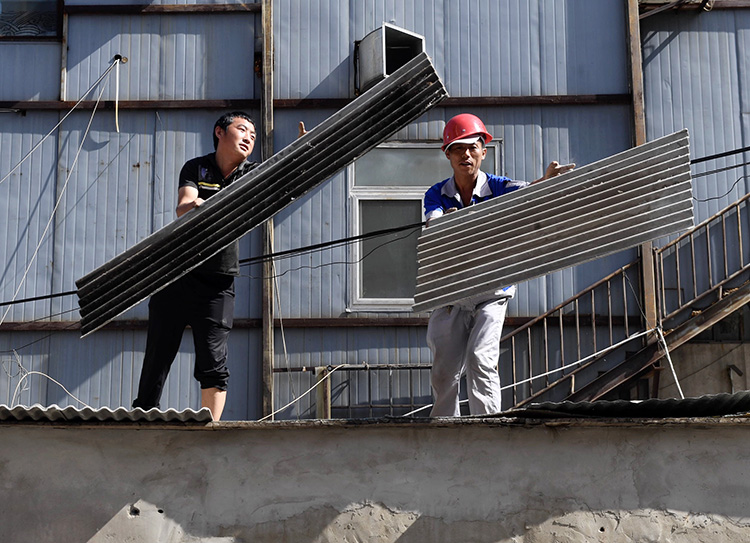 施工人員拆除違建房頂部的石棉瓦.