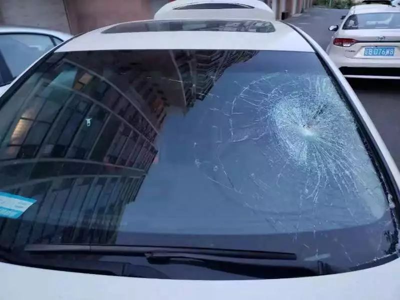 前挡风玻璃碎裂,车身局部凹陷,破坏者砸车用的理石地砖碎块就扔在车上