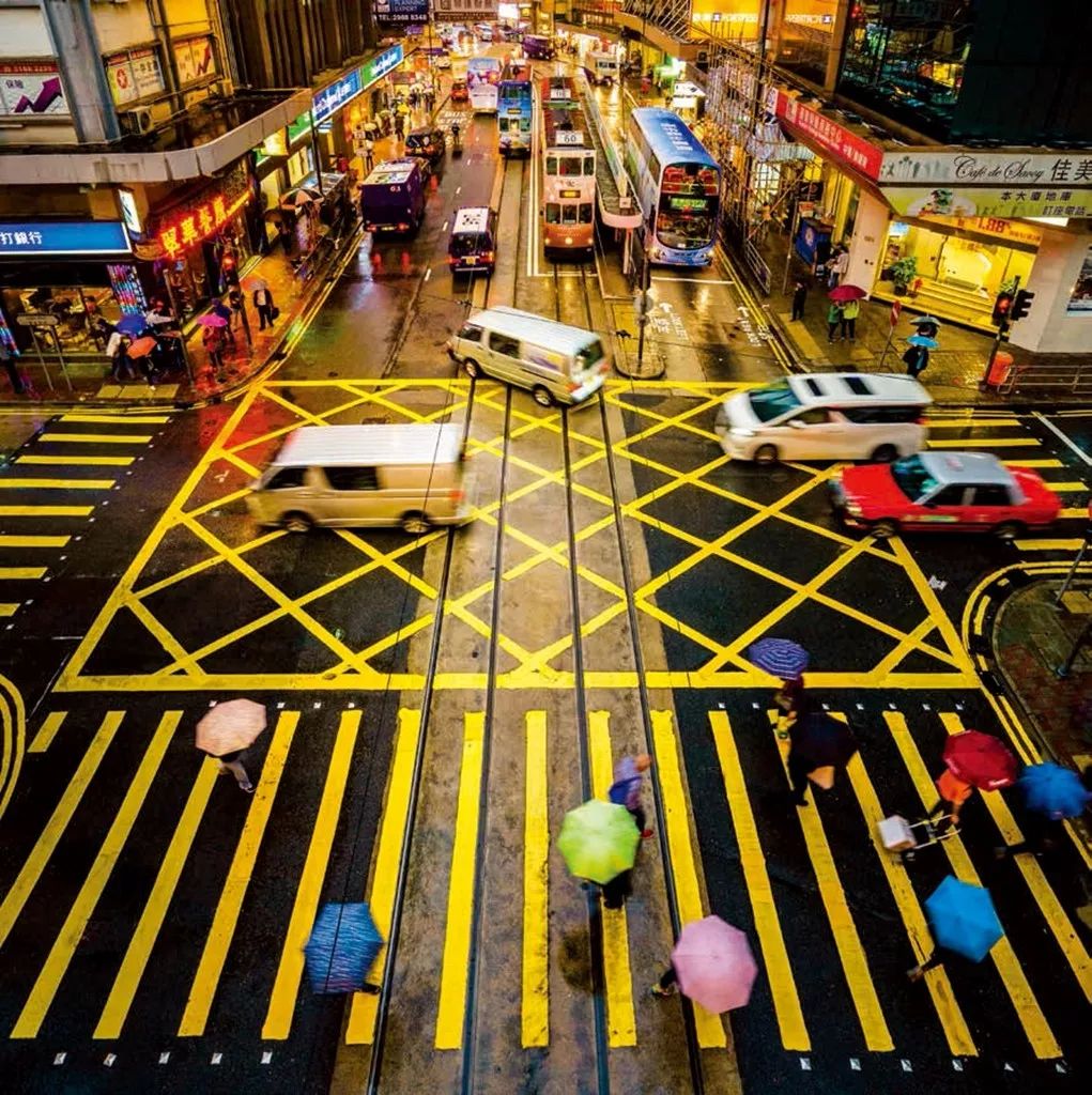 黄色的斑马线,五颜六色的雨伞和德辅道上商铺的灯光构成了一道充满