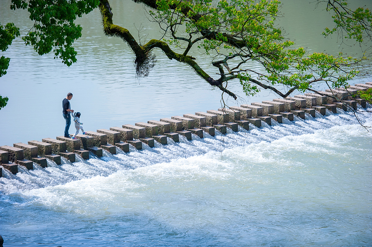 条用石墩整齐排列搭起的小石桥,游人一步跨越一个石墩,好似在走石碇步