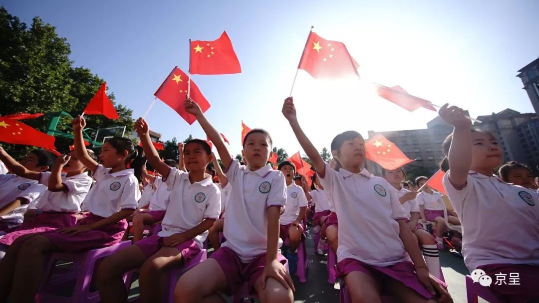 武警战士的身后,身穿少数民族服装的同学们和教师,手举小国旗边走边挥