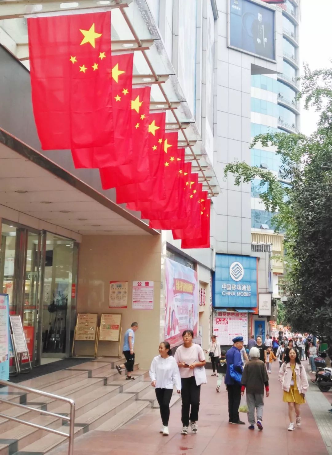 忠山公园五星红旗迎国庆△市民在摩尔商场前与国庆宣传标语合影