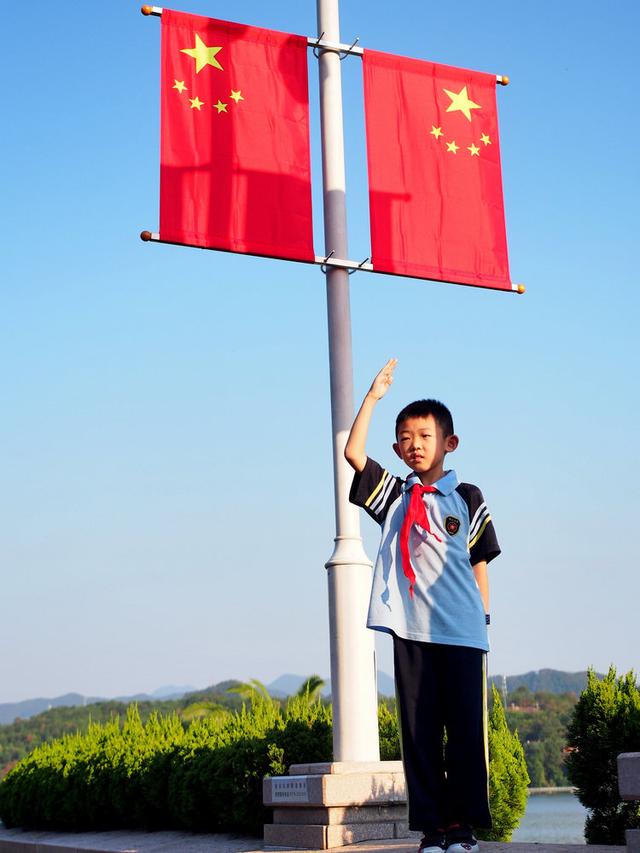 一個小男孩,正在五星紅旗下敬著隊禮,他媽媽正在幫他拍照.