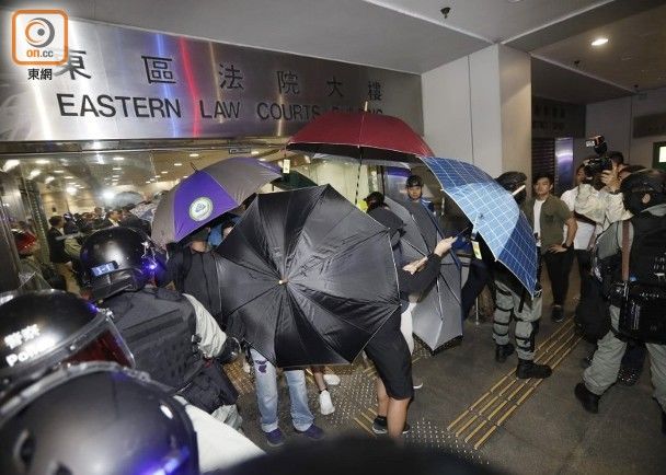 被告在雨伞遮挡下走出法院.图自香港"东网"