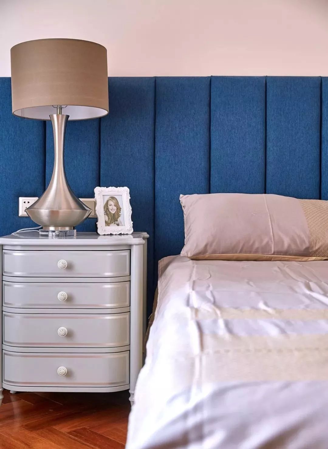 蓝色软包,银色床头柜,香槟色拉伸质感台灯,搭配柔和色乳胶漆墙面