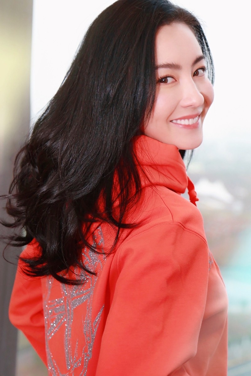 照片中,张柏芝身着橘红色印花连帽卫衣,一头乌黑浓密的微卷长发与粉嫩