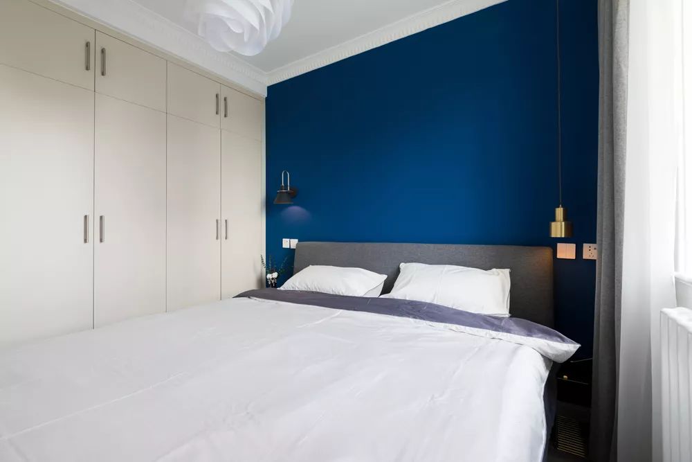 卧室以深蓝色的背景墙,搭配一张灰色布艺床,床头两侧都做了吊灯,布置