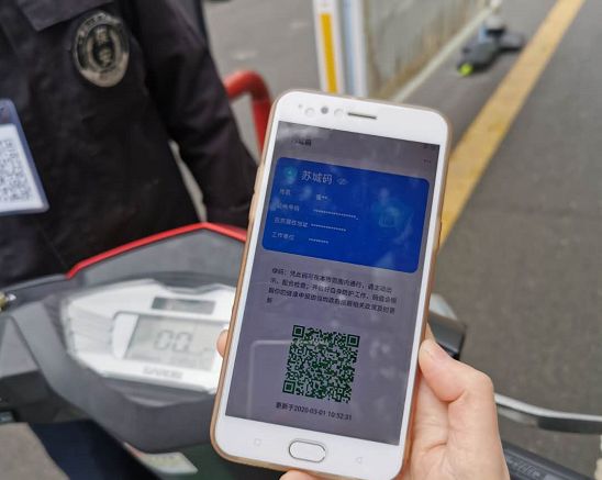 在小区门岗卡口,社区工作人员对进入小区人员进行体温监测,并要求出示