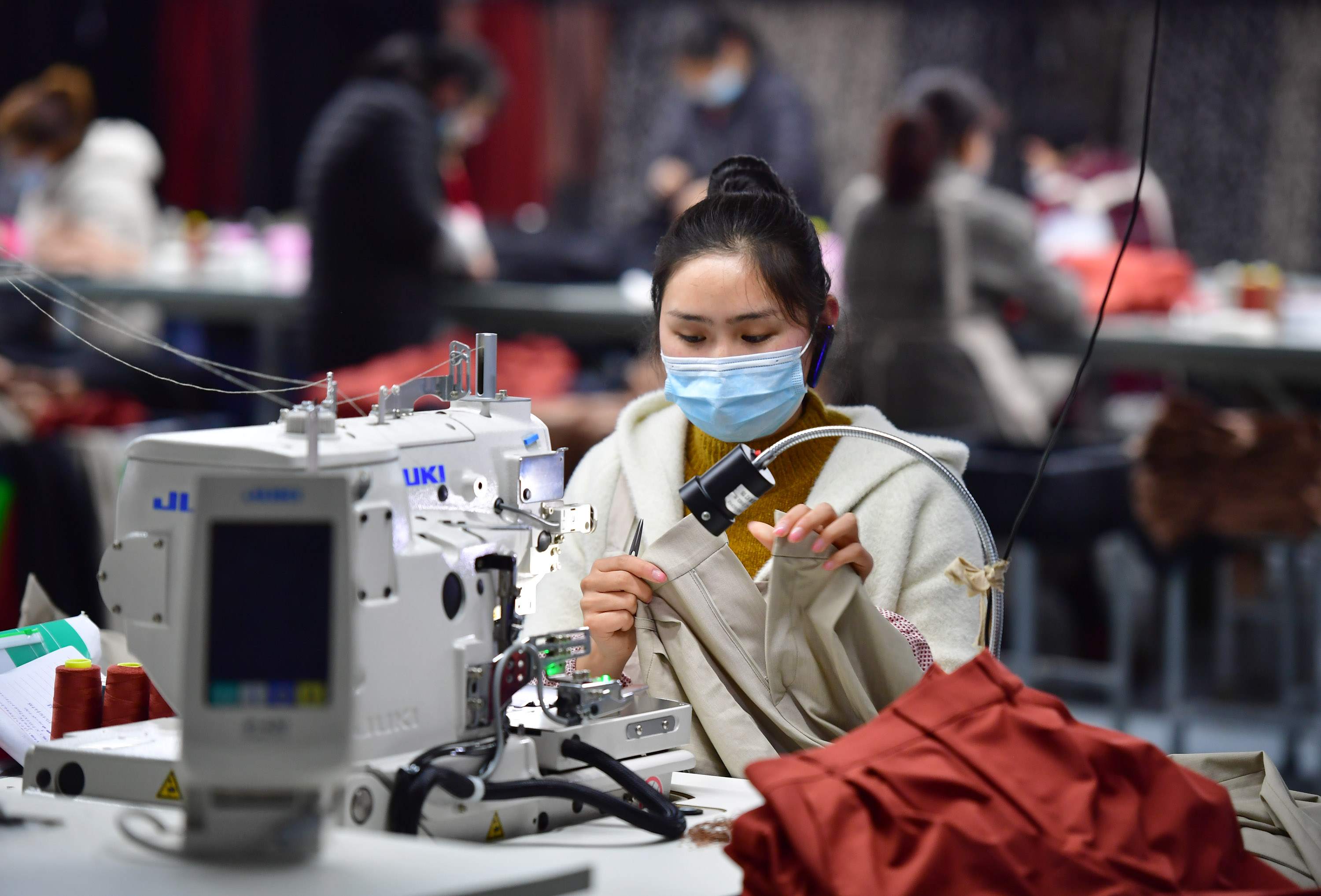 3月11日,在城固县博望街道办事处江湾社区一服装厂内,工人在缝制服装