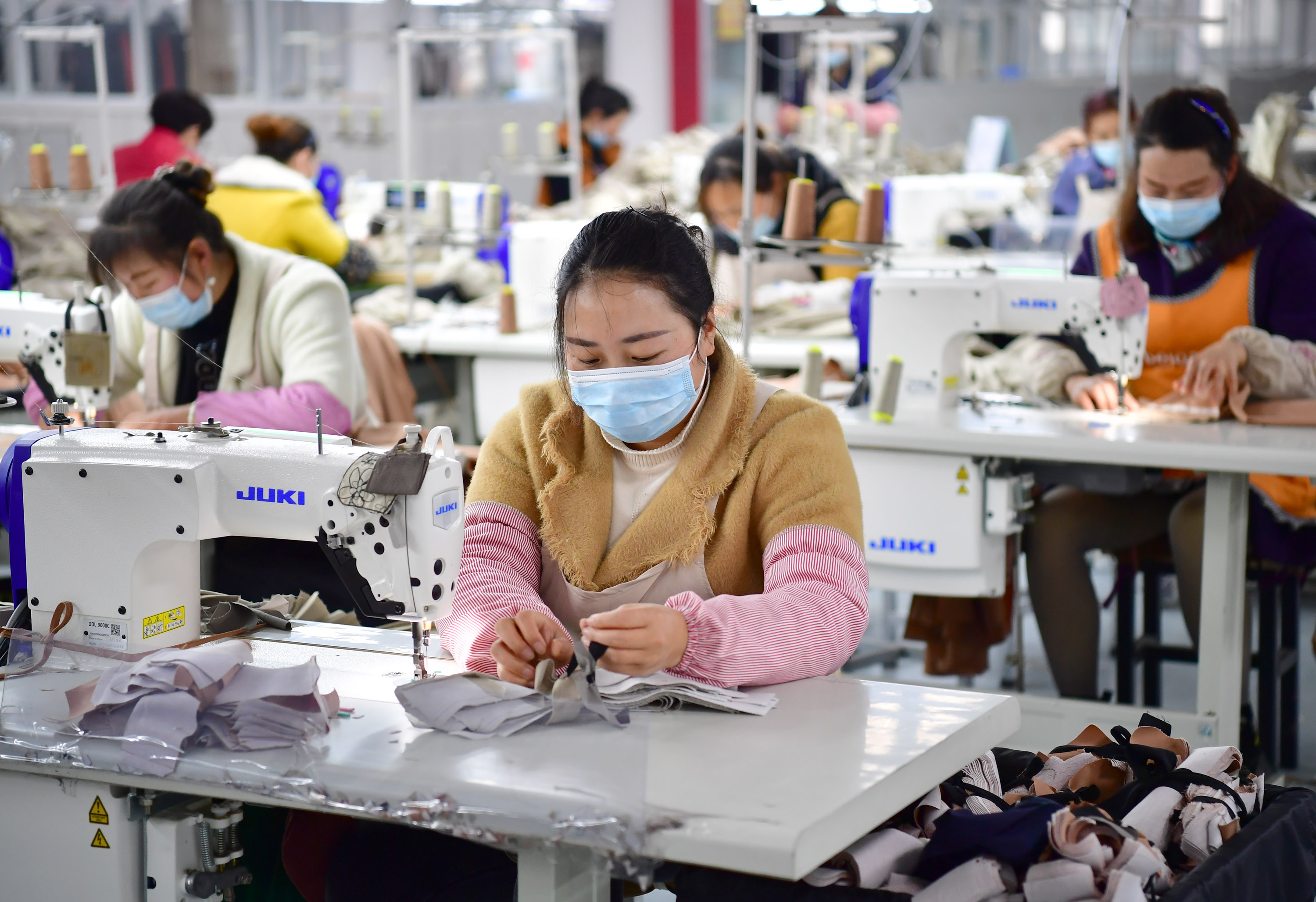 3月11日,在城固县博望街道办事处江湾社区一服装厂内,工人在缝制服装