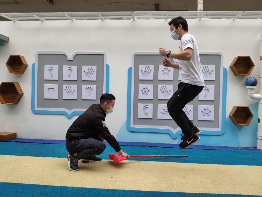 摆钟障碍跳玩法:家长横握扫把并且左右摆动扫把,幼儿双脚跳过扫把