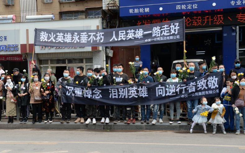 现场群众在道路两侧摆放菊花,并举起横幅:"你们用生命换来凉山人民