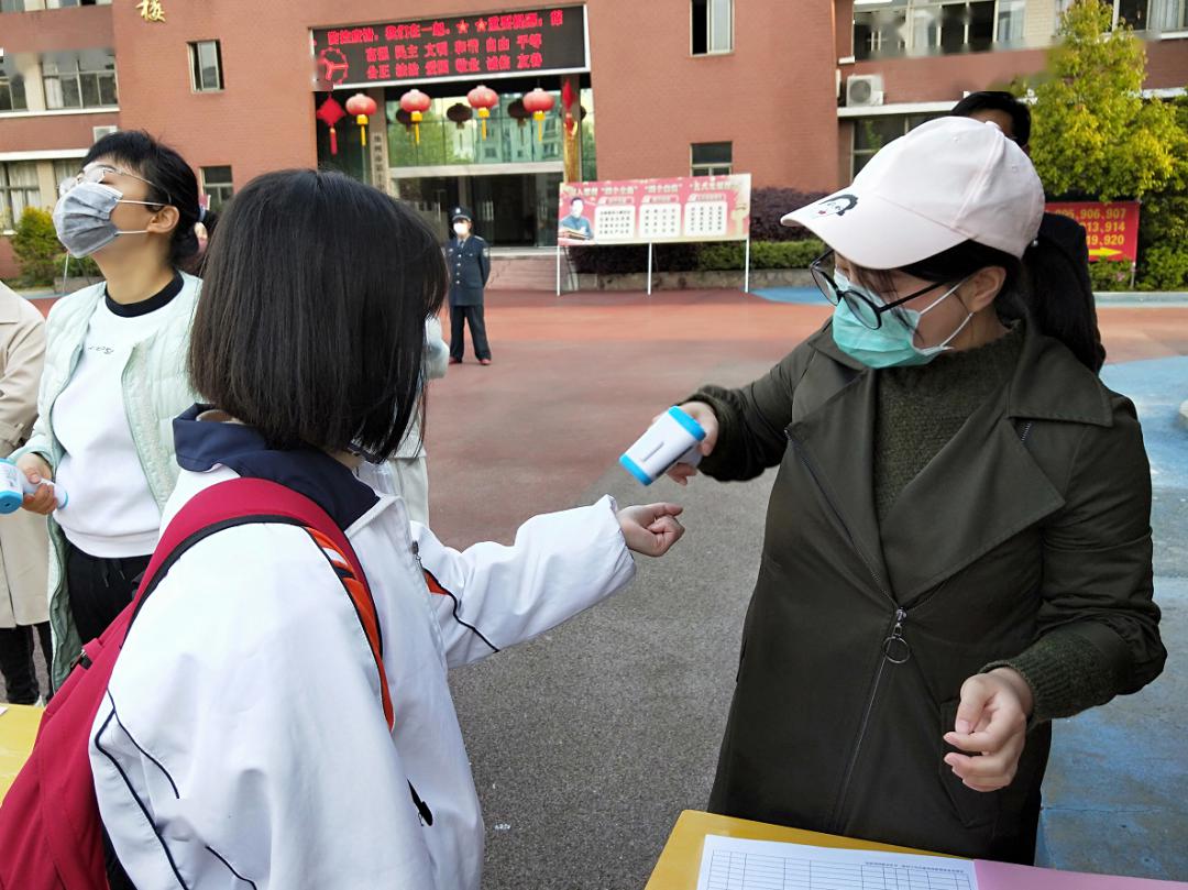 学生们身穿校服,佩戴口罩,有序走近校门,经过校门口的红外线自动测温