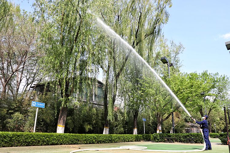 消防员手持水枪对杨柳树喷水.