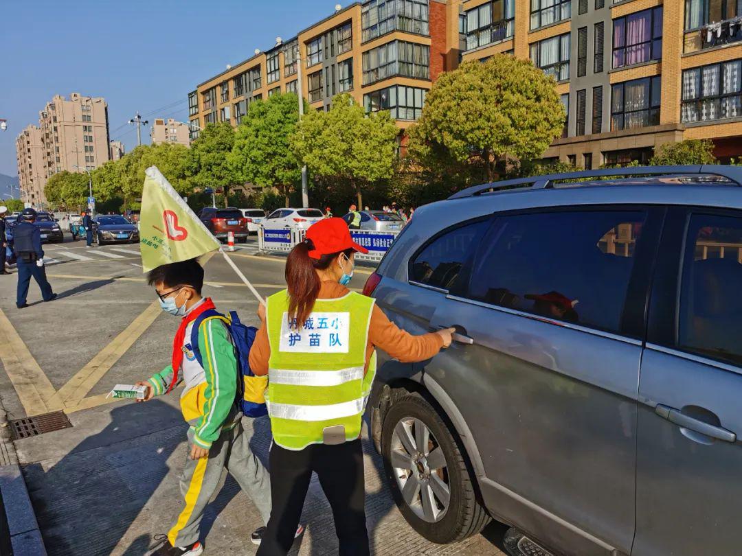 学校门口,保安,家长护苗队指挥着家长车辆有序停放,县教育局局长胡海