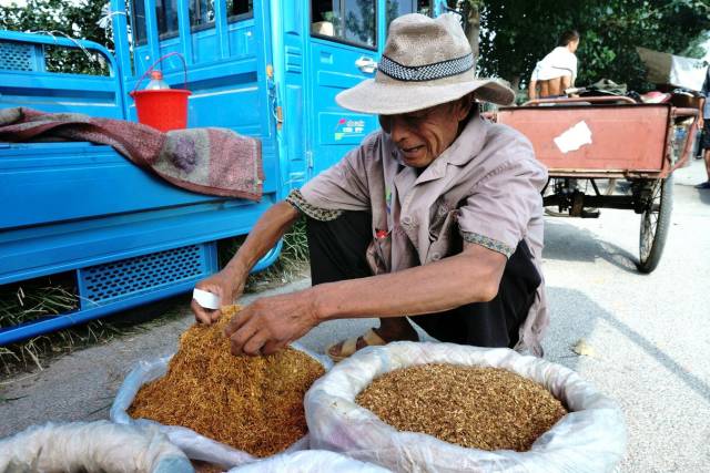 一位老妈妈在品尝摊主给她介绍的旱烟.