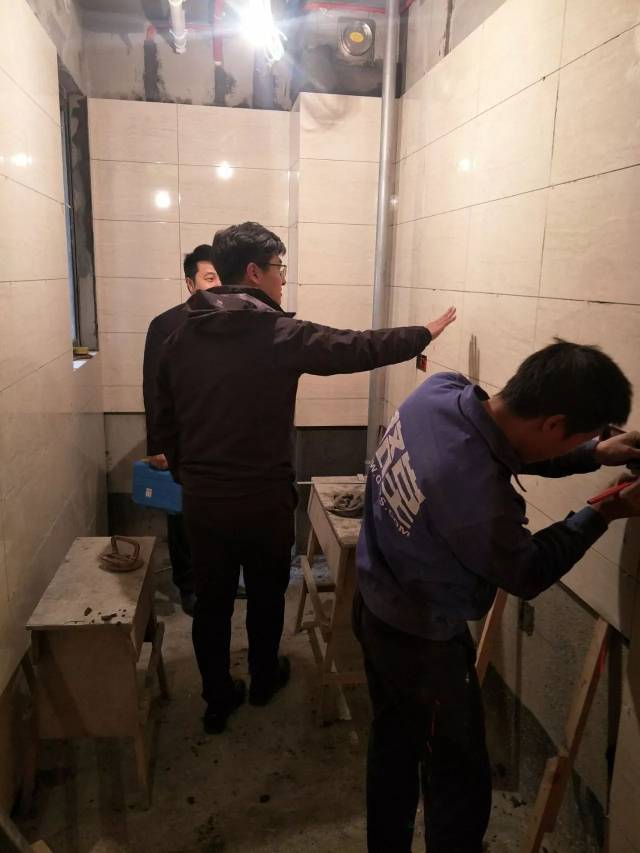 泥工师傅正在厨房认真贴墙砖,巡检组认真检查施工工艺,很规范.
