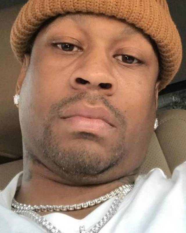 艾弗森坐在车上,带着帽子,表情慵懒,两个钻石耳钉和银色项链非常亮眼.