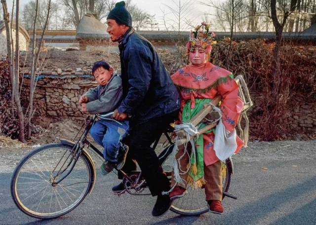 村民骑着自行车驮着儿子兴高采烈地去送媳妇参加高跷秧歌会