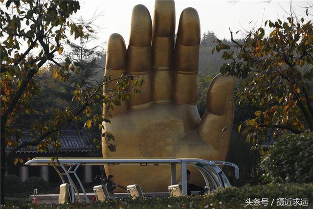 游客抚摸77米高佛手雕塑,据说能增寿添福