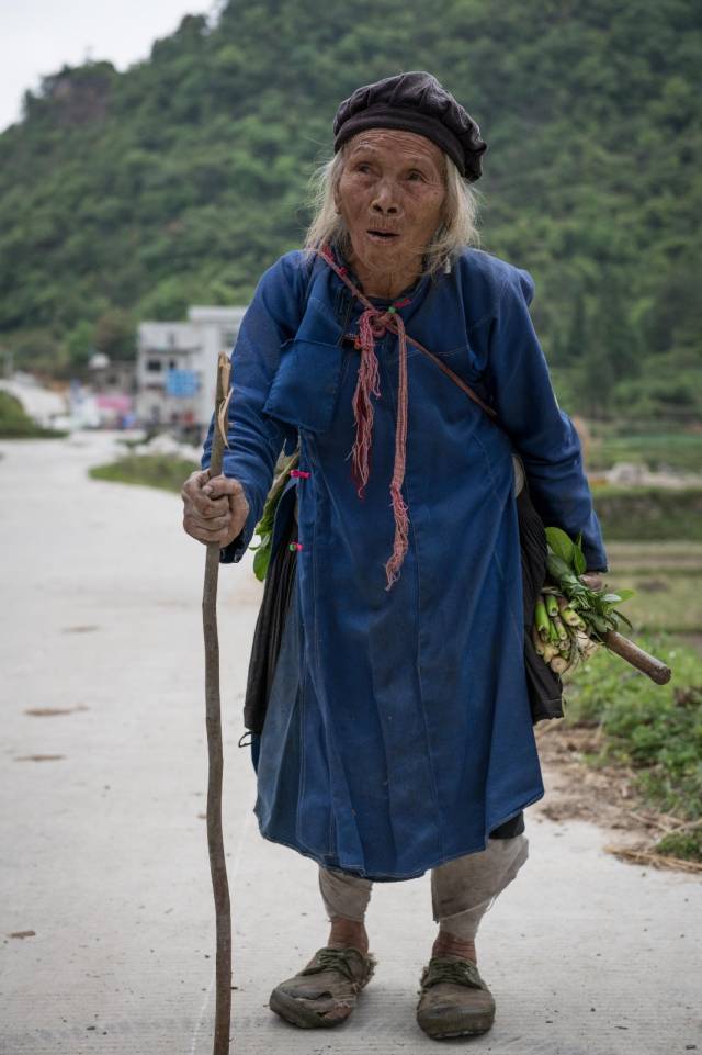 老奶奶刚从田间回来,她手里的拐杖也是从附近的树上弄的树枝,面对镜头