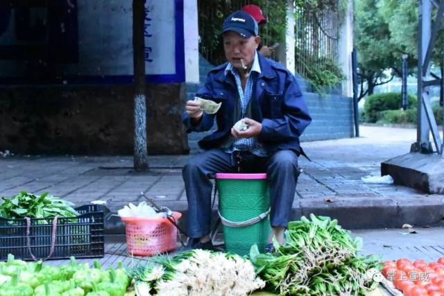 这位爷爷正在给前来买菜的顾客找钱,嘴里还抽着自己制作的烟卷,看起来