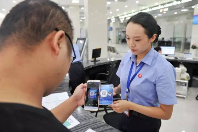 人口与出入境服务大厅内市民拿出手机扫描二维码进行网上预约办理业务