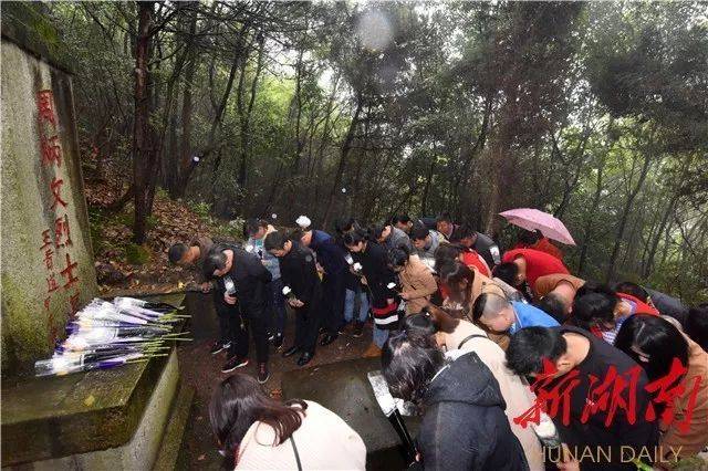 雨衣,手捧鲜花,徒步走过崎岖湿滑的山路,来到革命烈士周炳文的墓碑前