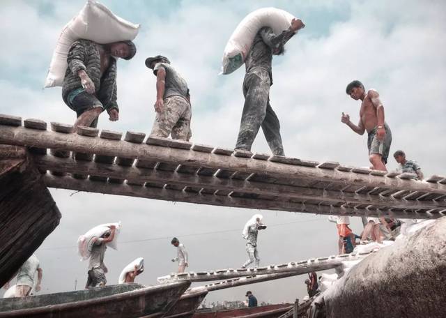 张家勇 作品简介:码头工人通过踏板把货物搬运到岸边的小货车,一条条