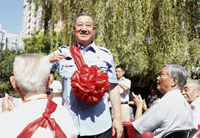 东花市街道居民中的退伍军人佩戴大红花坐在最前排并依次向居民敬礼致